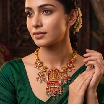 South Indian bride wearing an antique gold Lakshmi temple necklace with ruby stones, polki diamonds, emerald beads, and jasmine flower hairstyle in green silk saree.