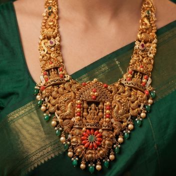 South Indian woman wearing an antique gold temple hararam necklace with Lakshmi pendant, green beads, pearls, and traditional jasmine hairstyle in green silk saree.